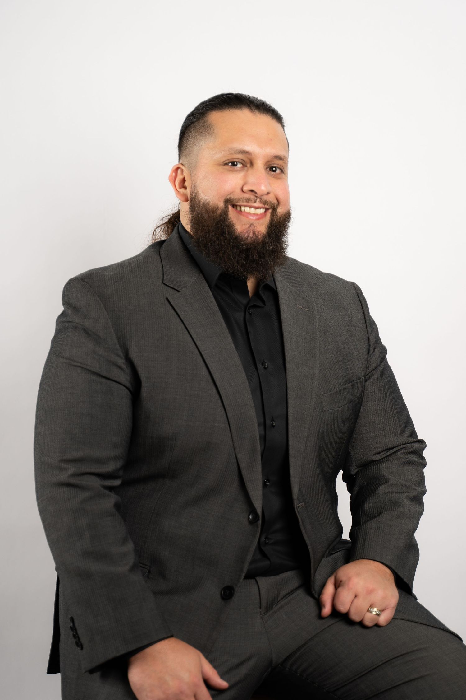 Professional headshot of person in grey suit with beard against white background.
