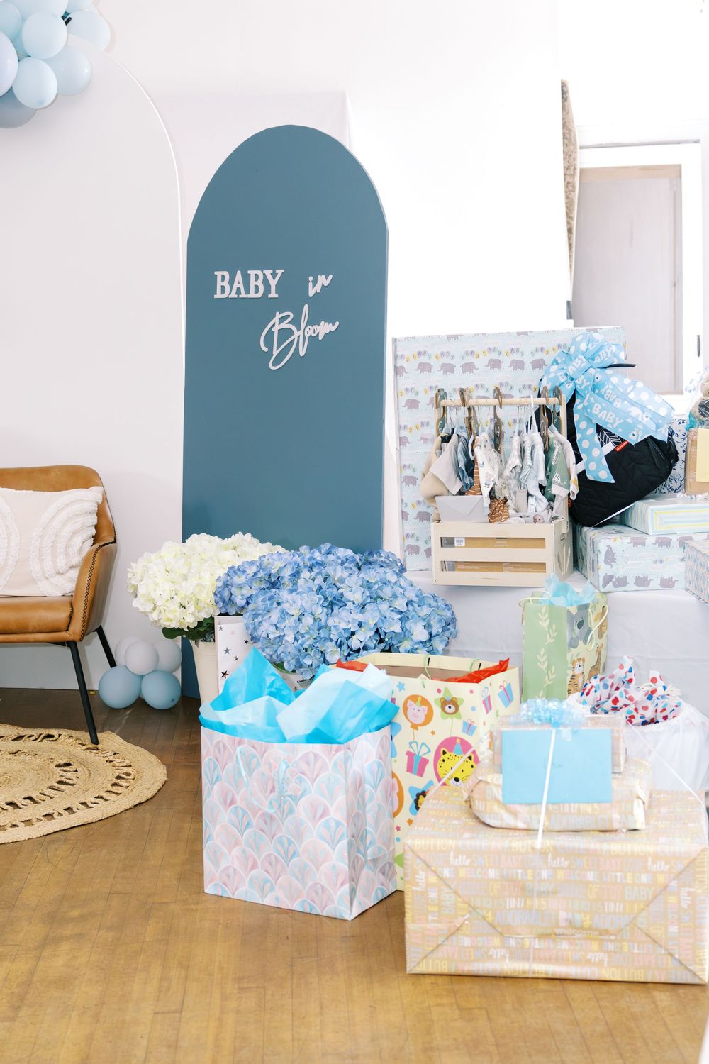 Baby in Bloom blue arch backdrop surrounded by gift bags, boxes, and blue hydrangeas at baby shower.