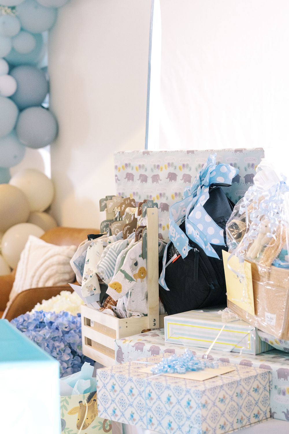 Stacked baby shower gifts and wooden crate filled with baby items and blue elephant wrapping paper.