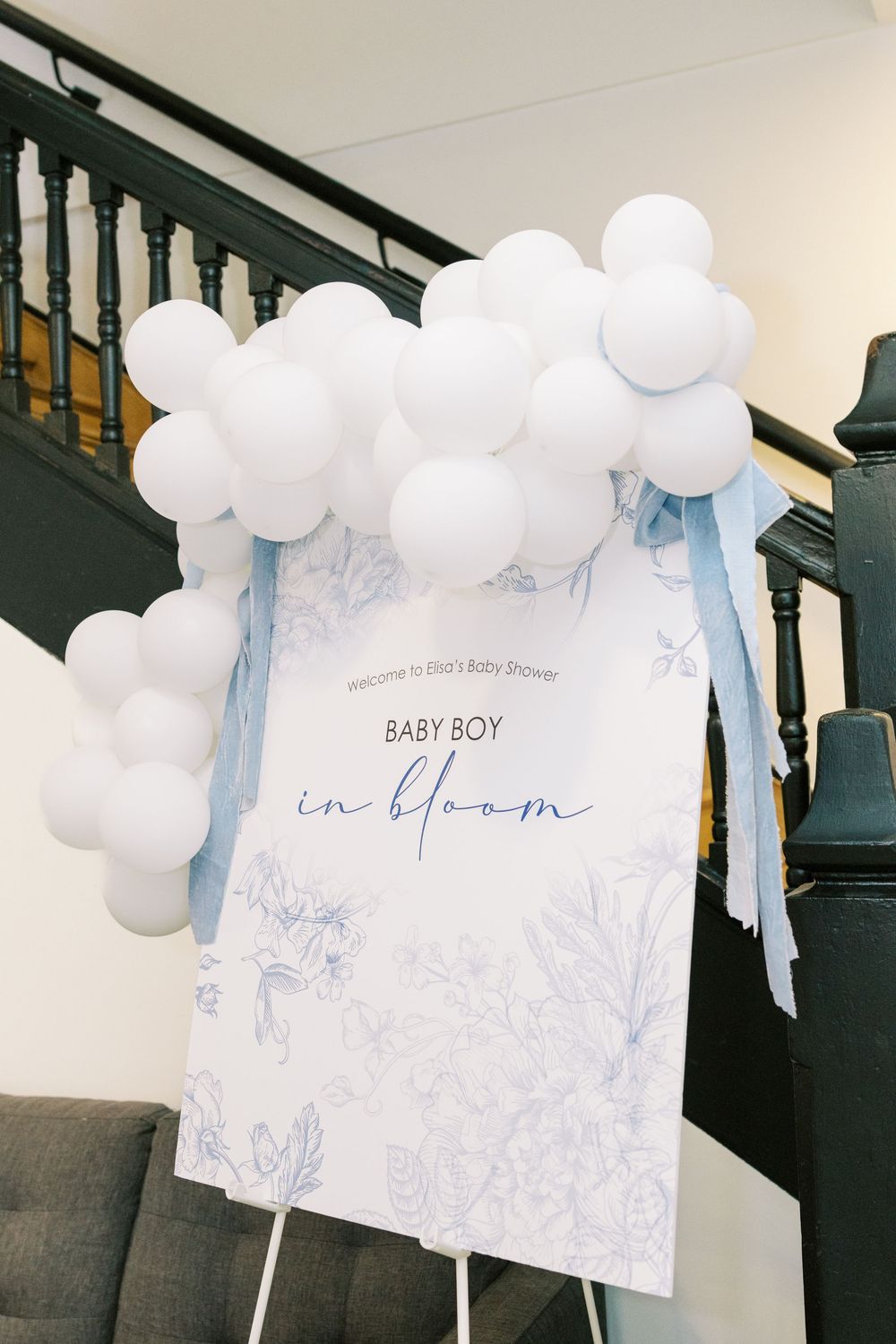 White balloon garland arch framing a Baby Boy in Bloom welcome sign at a baby shower entrance.