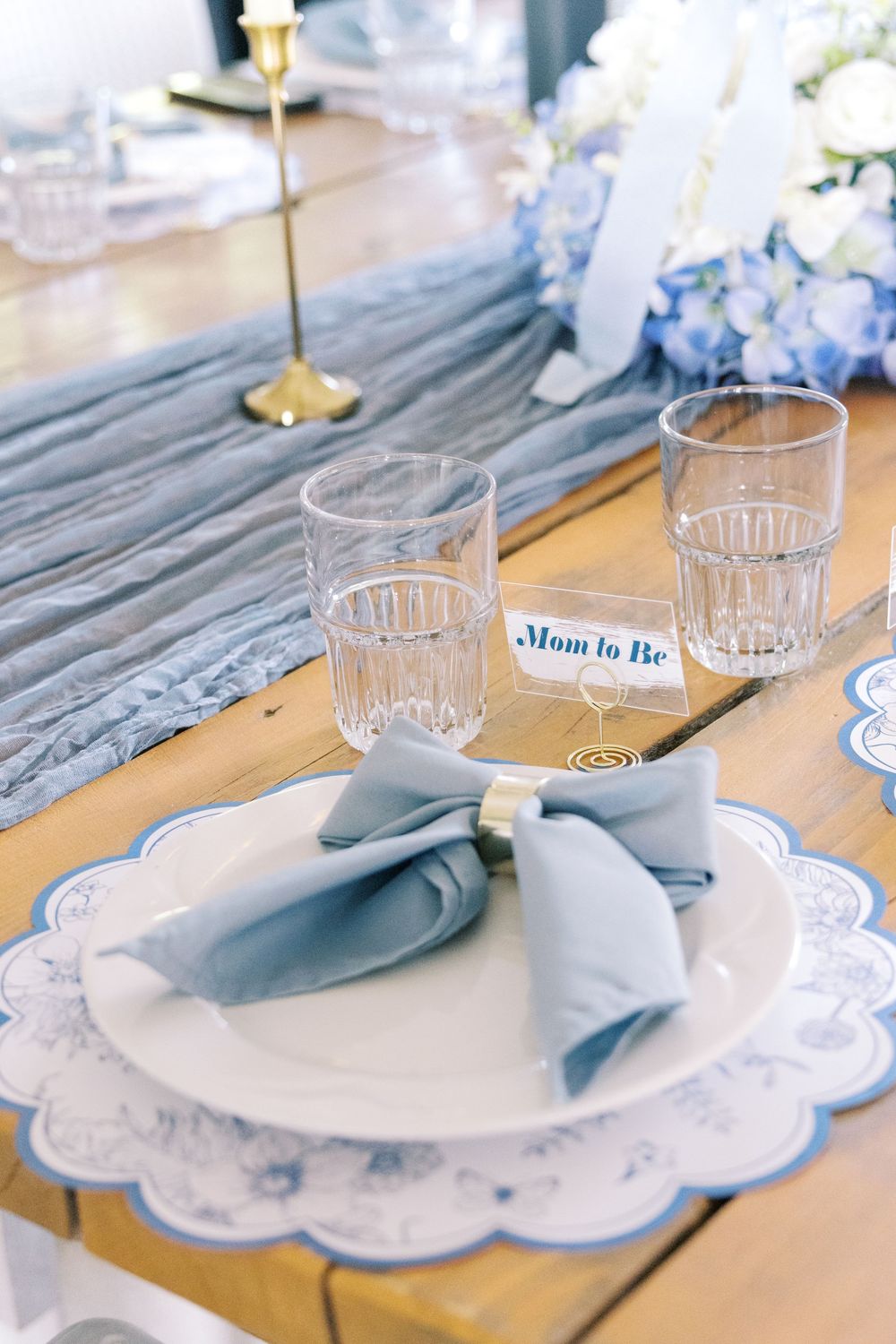 Elegant baby shower place setting with blue napkin, scalloped placemat, and Mom to Be name card.