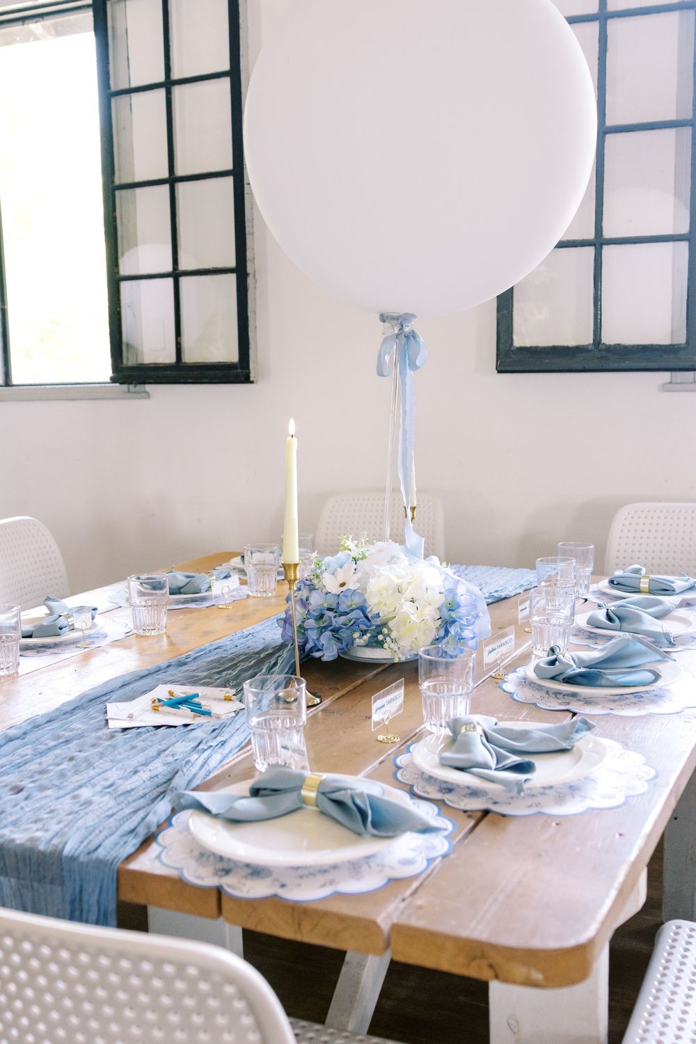 Baby shower dining table with blue runner, white balloon centerpiece, hydrangeas, and candle.