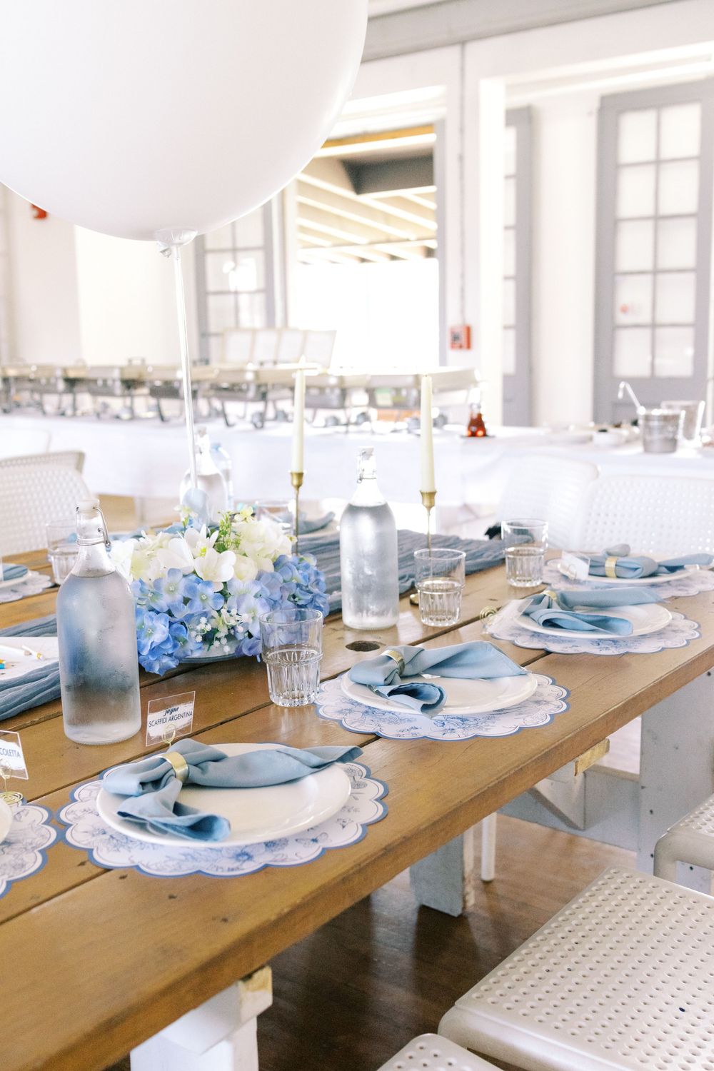 Elegant blue and white table setting with hydrangeas, scalloped placemats, and a large balloon centerpiece on a wooden table.