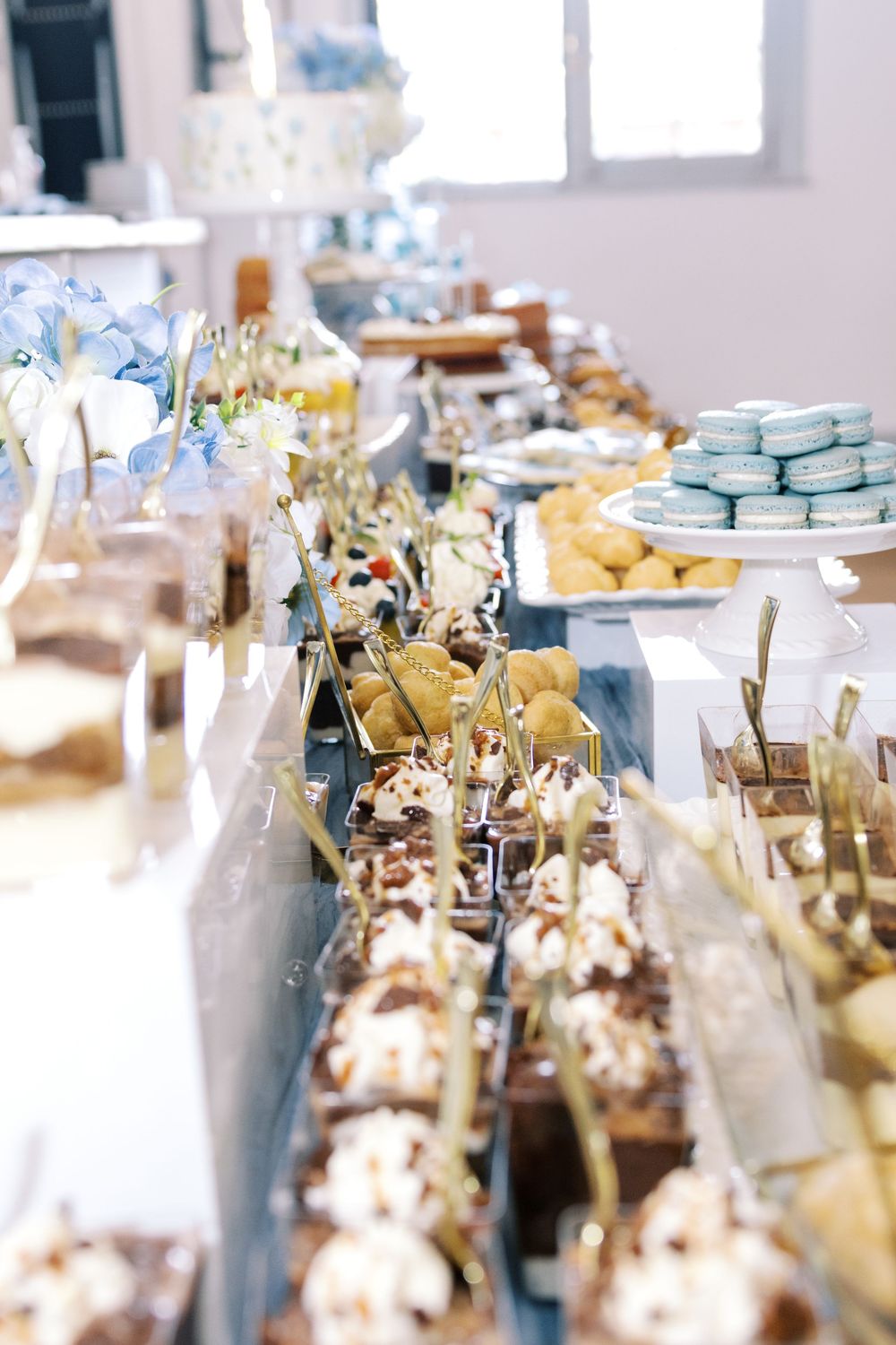 Elegant dessert bar display with chocolate cups, macarons, cream puffs, and assorted mini desserts for a blue-themed celebration.