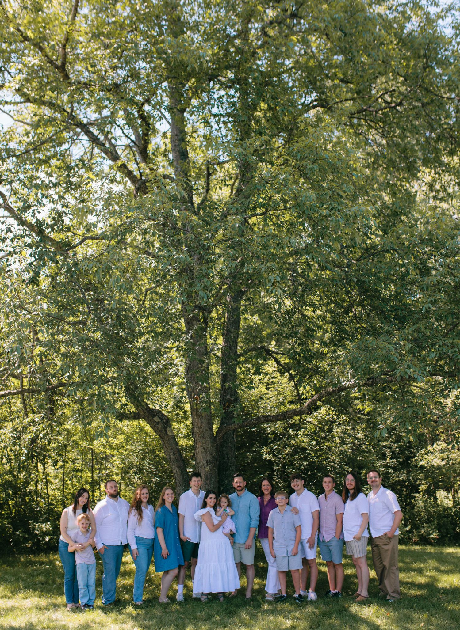 Family portrait session captured outdoors with a natural backdrop of lush green trees in summer lighting.