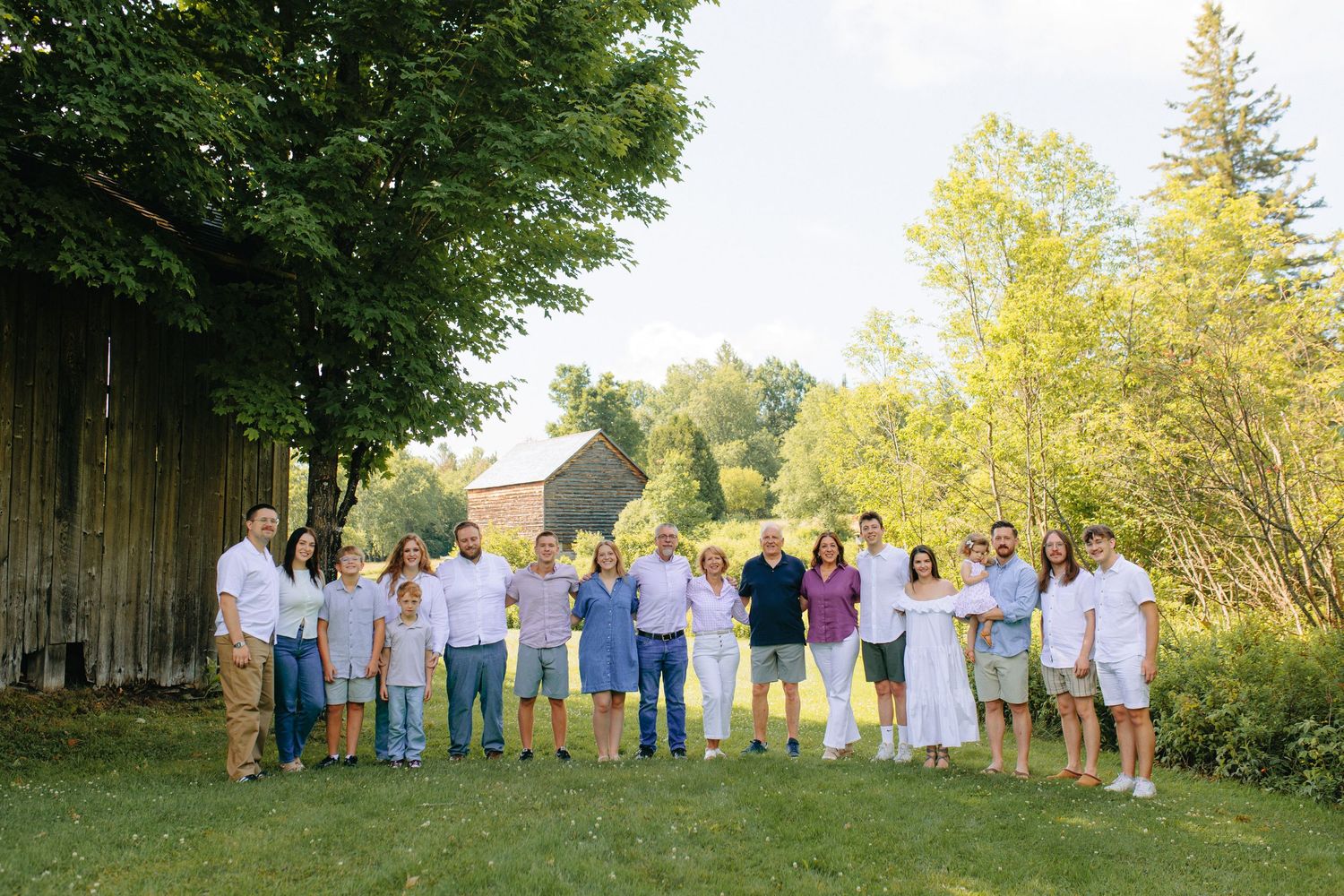 A group gathers for a casual outdoor photo by a rustic barn on a sunny summer evening.