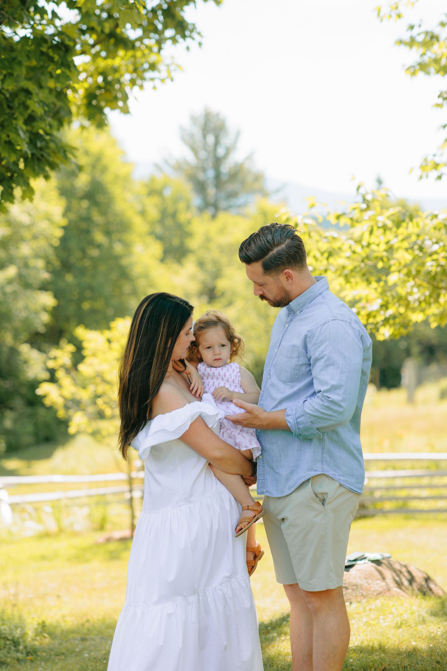 A family enjoys a tender moment together on a sunny summer day in a lush green park setting.