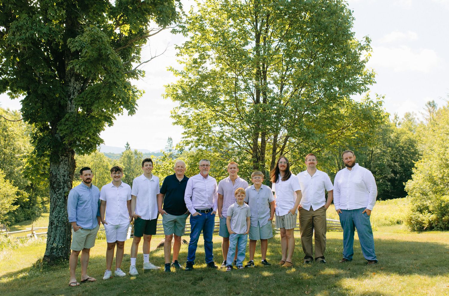 Group of people in coordinating casual outfits gathered outdoors on a grassy hillside on a sunny summer day.