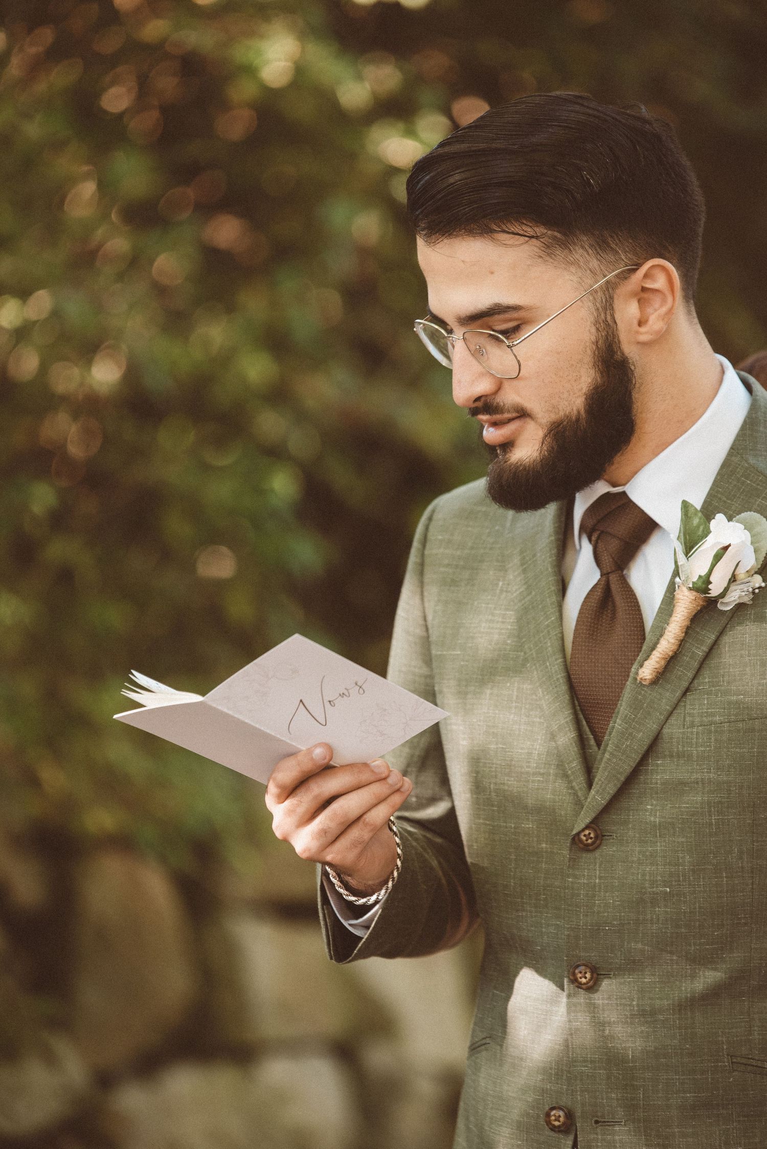 A man wearing a green suit reading from a vow book on his wedding day.