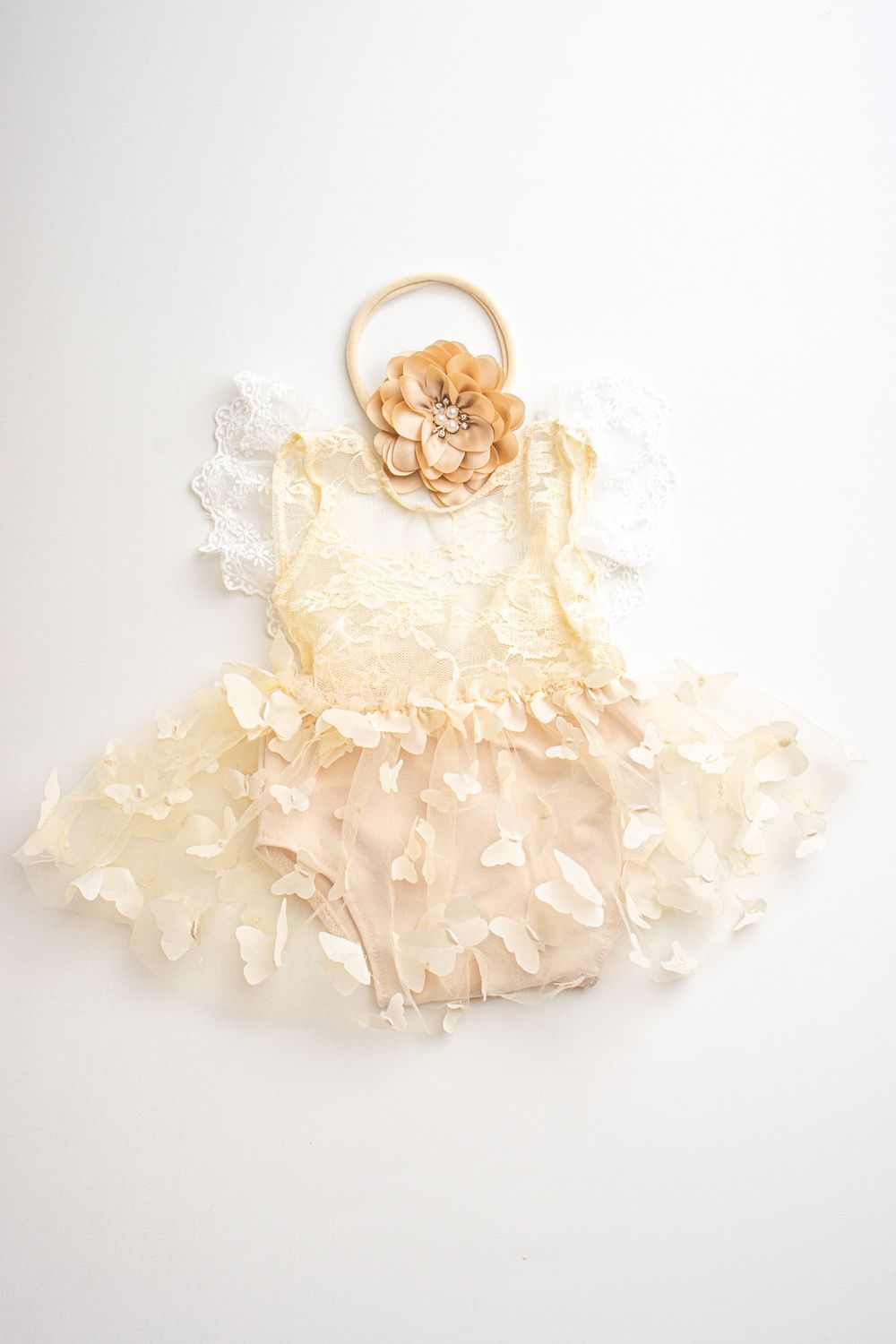 Delicate ivory lace baby dress with ruffled layers and peach flower headband laid flat on white background. newborn fotografie almere