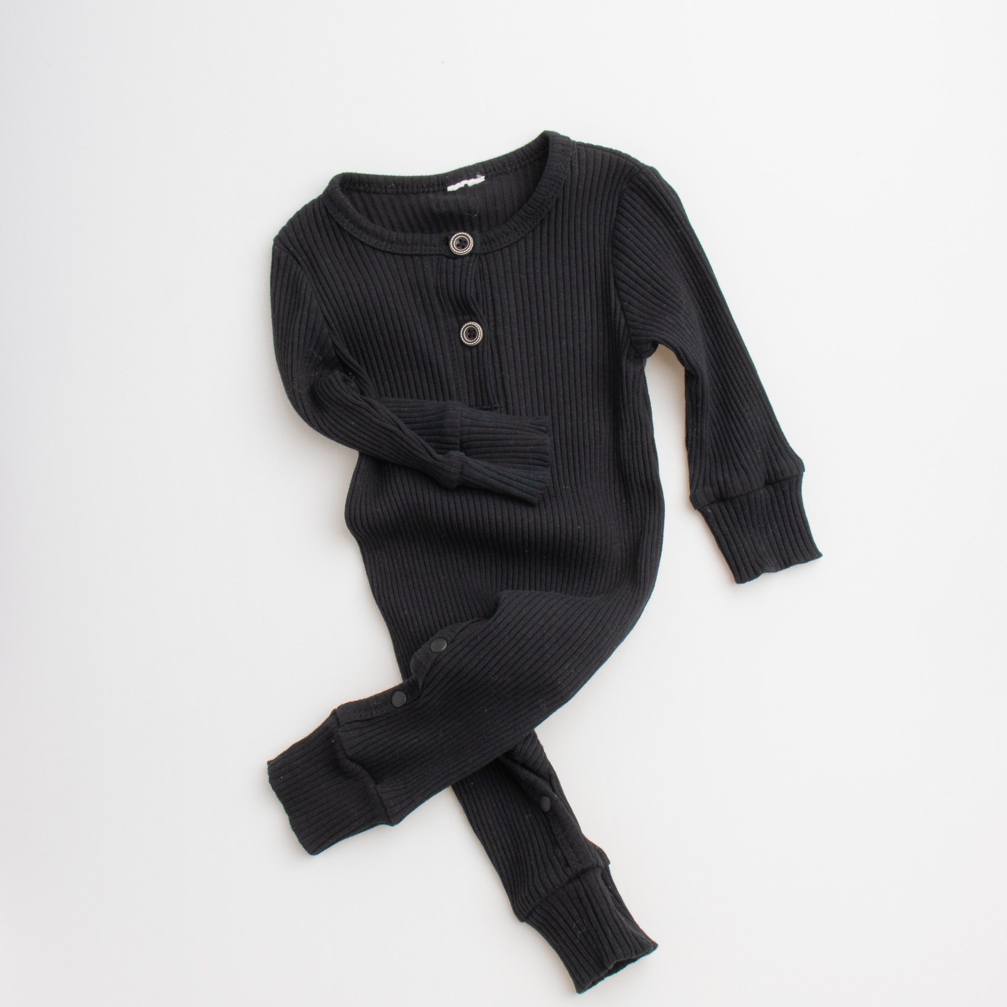 Black ribbed knit baby romper with long sleeves and button details laid flat on white background.