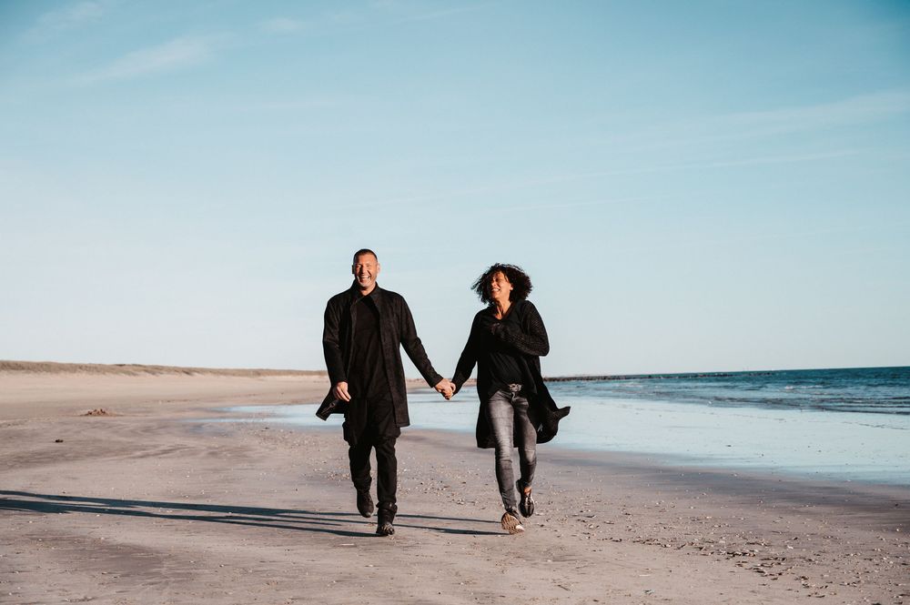 Farbfoto eines Paares bei Sonnenuntergang am Strand in Dänemark. Sie laufen Hand in Hand auf die Kamera zu, warmes Licht, Naturfotografie .