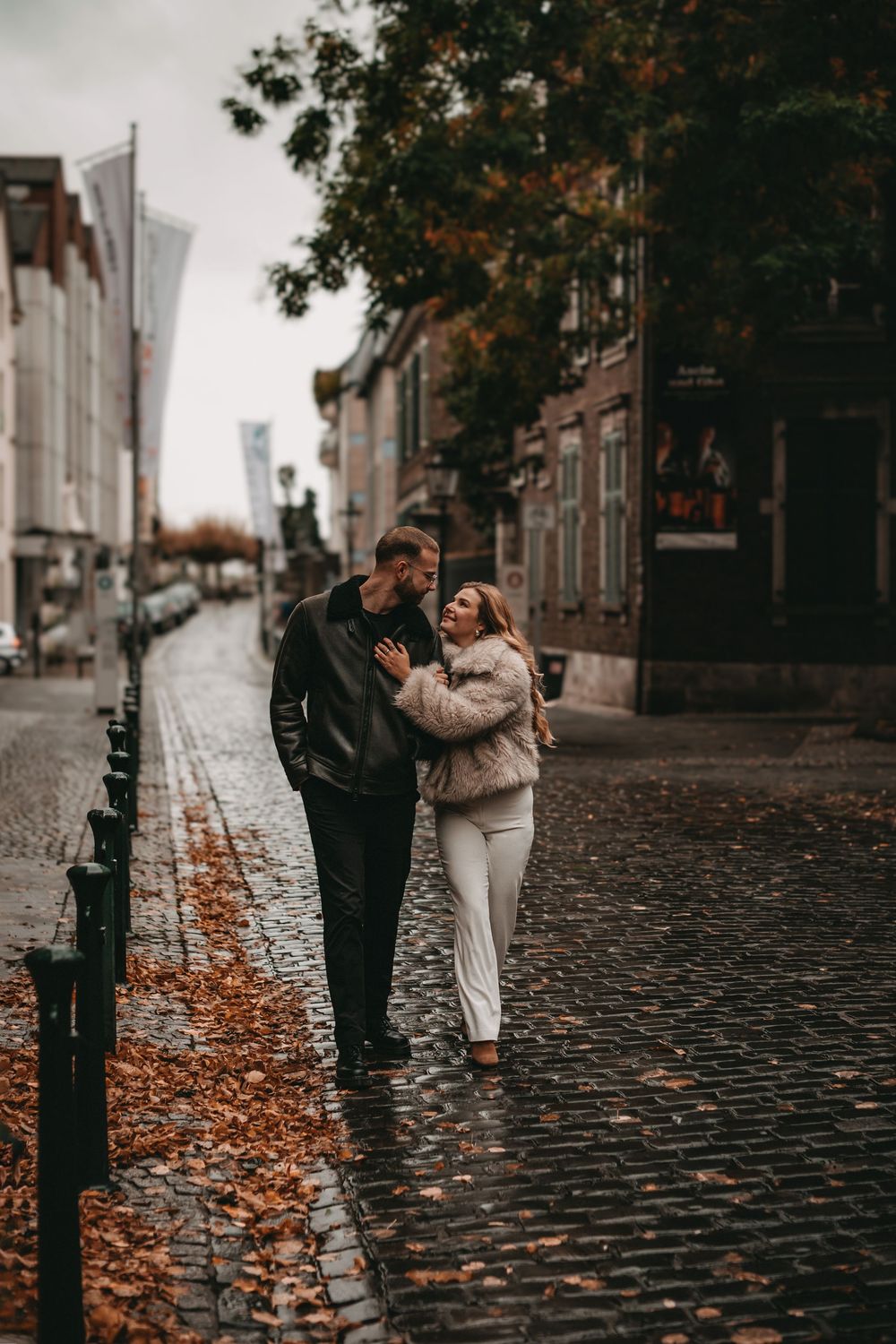 Verliebtes Paar läuft durch die Düsseldorfer Altstadt über nasses Kopfsteinpflaster mit Herbstlaub – romantisch, natürlich, herbstlich.