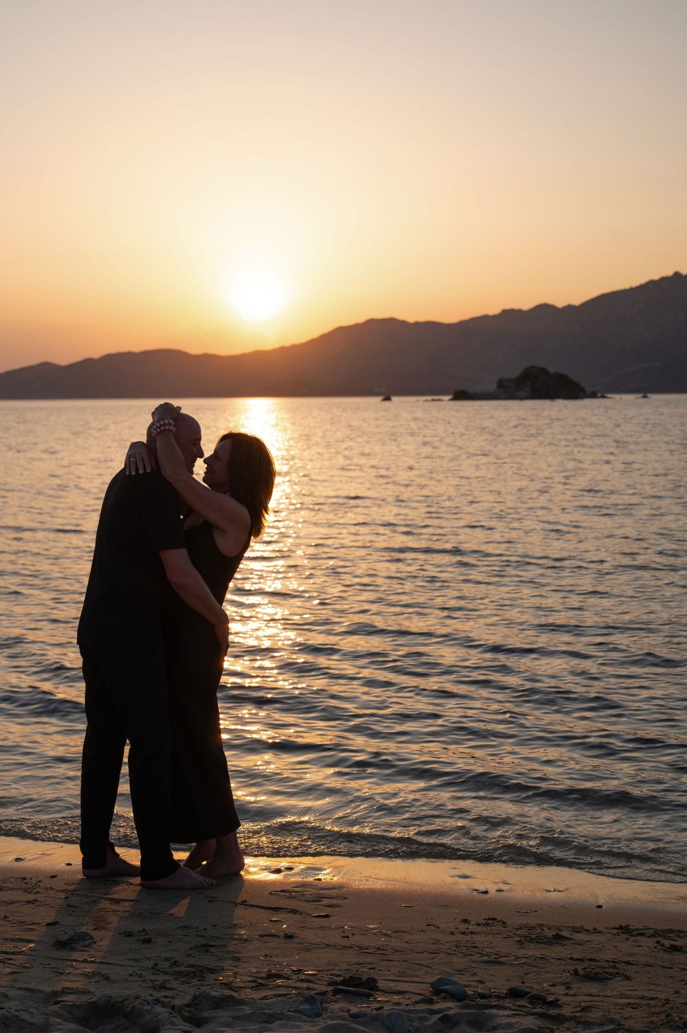 Romantischer Moment auf Sardinien: Ein Paar umarmt sich am Meer im goldenen Sonnenuntergang – Liebe und Emotion in warmem Licht.