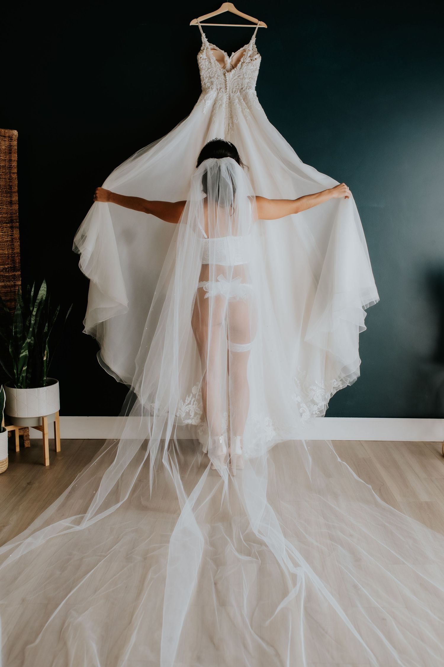 Elegant white wedding dress and flowing train hanging against dark teal wall during a bridal boudoir session by tucson boudoir photographer