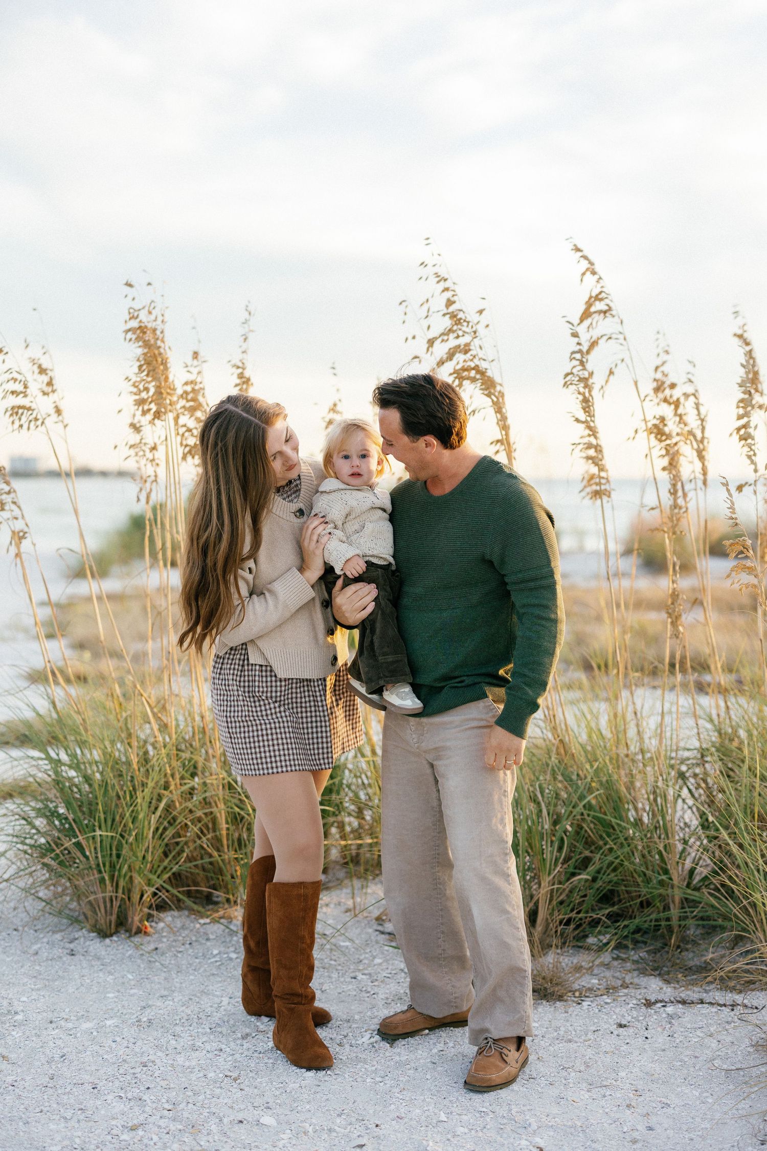A family poses together in a natural forest setting wearing casual clothing in white and green tones.