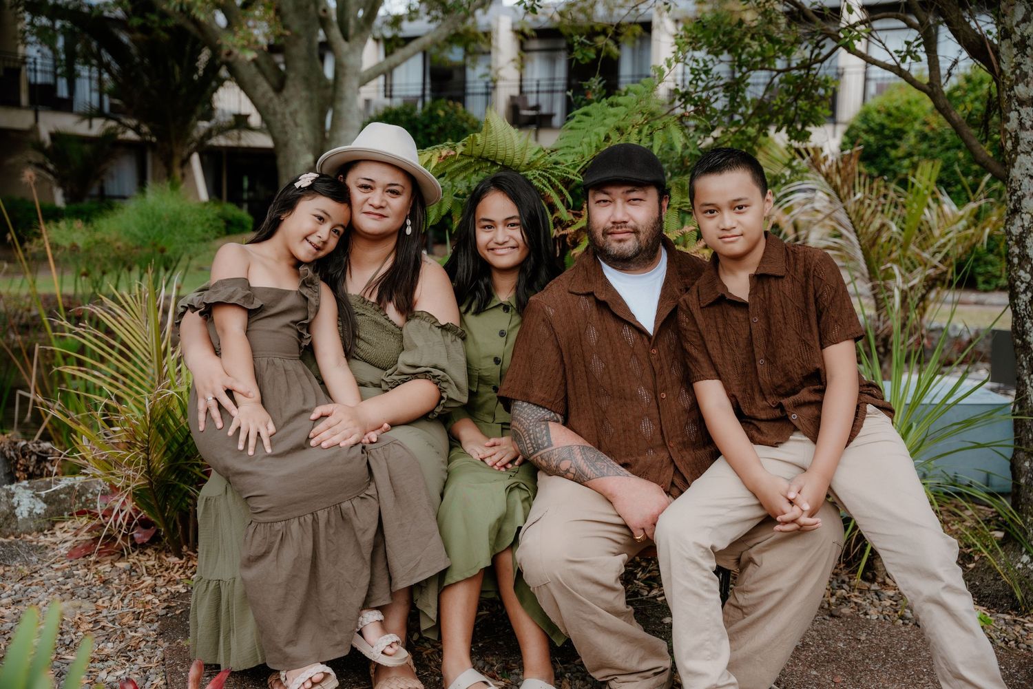 A cheerful group in coordinated earth-toned outfits sits together on garden steps surrounded by lush greenery.