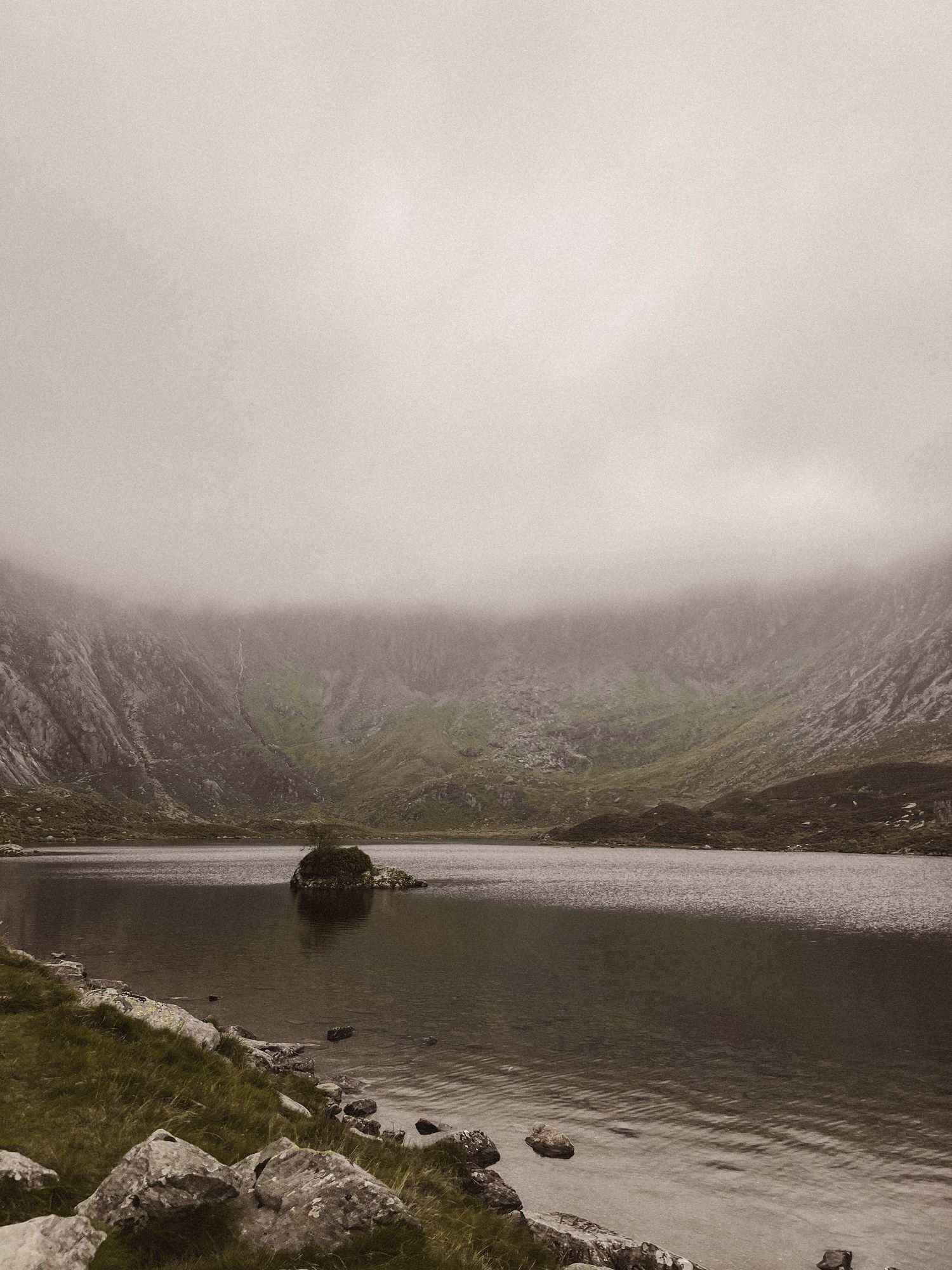 A misty mountain waterfall cascades down rocky terrain in moody weather conditions, creating a dramatic landscape in Snowdonia.
