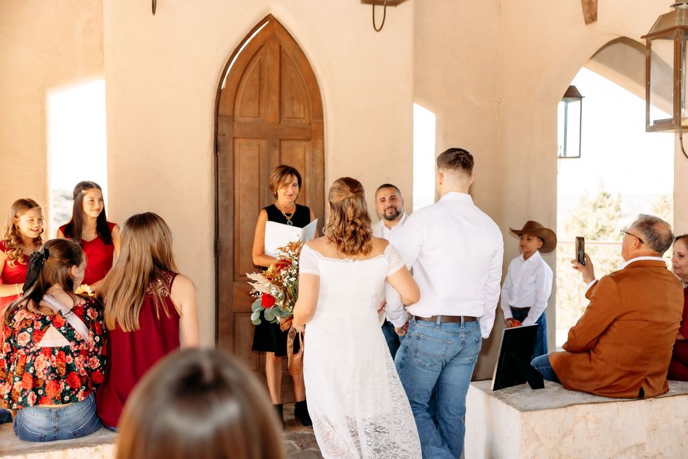 Group of people standing in a sunlit hallway with rustic wooden doors and white walls.