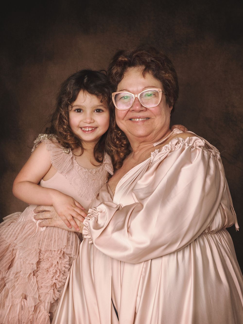 A studio-style portrait featuring matching pink dresses against a brown background in formal photography setting.