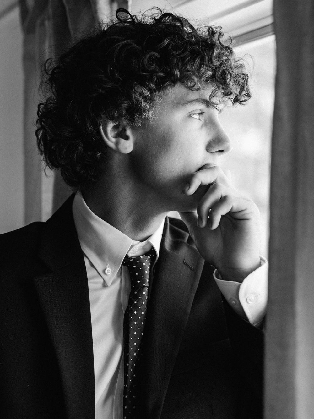 Artistic black and white portrait series showing a sharp suited figure with curly hair in dramatic shadow and light.