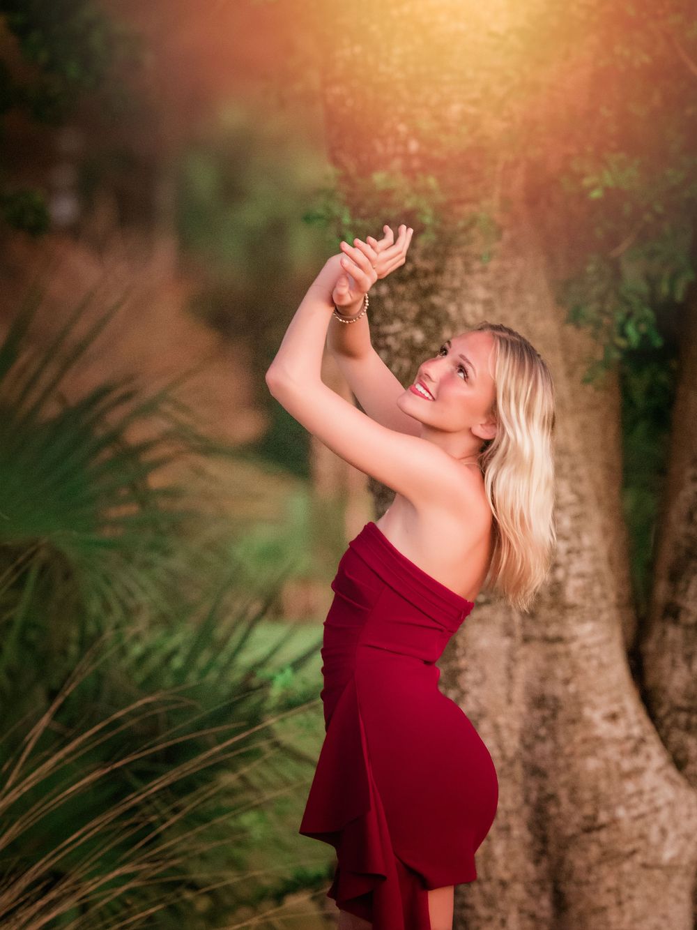A person in a red dress dances joyfully in a sunlit garden setting with palm fronds and trees in the background.