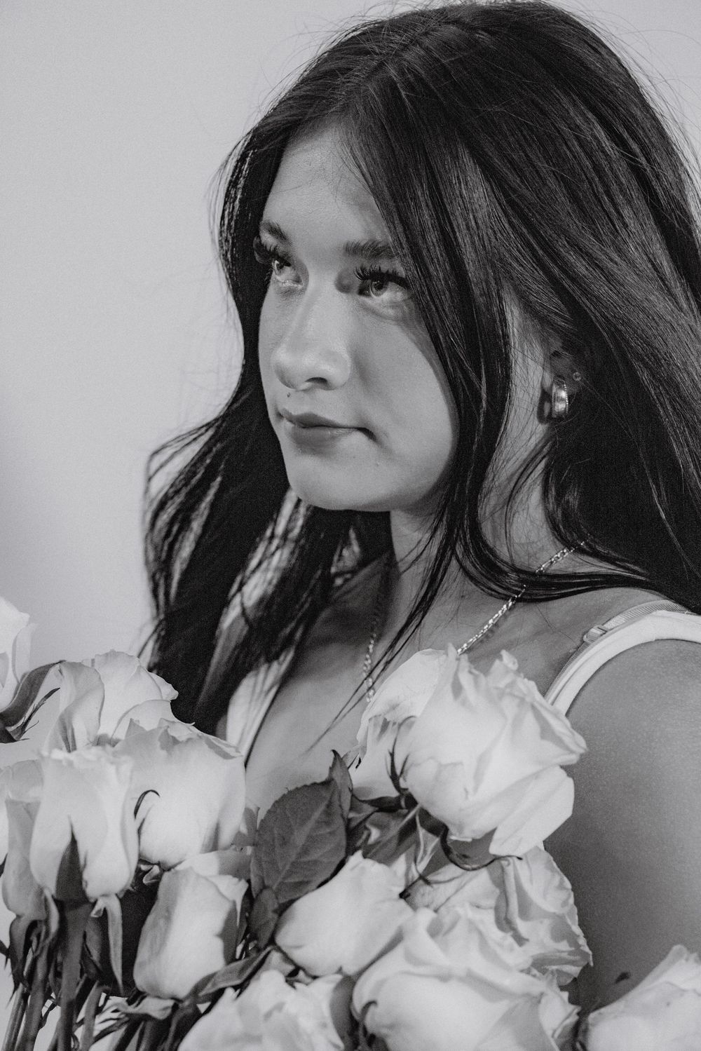 Black and white portrait photograph featuring long dark hair and white roses in an artistic composition.