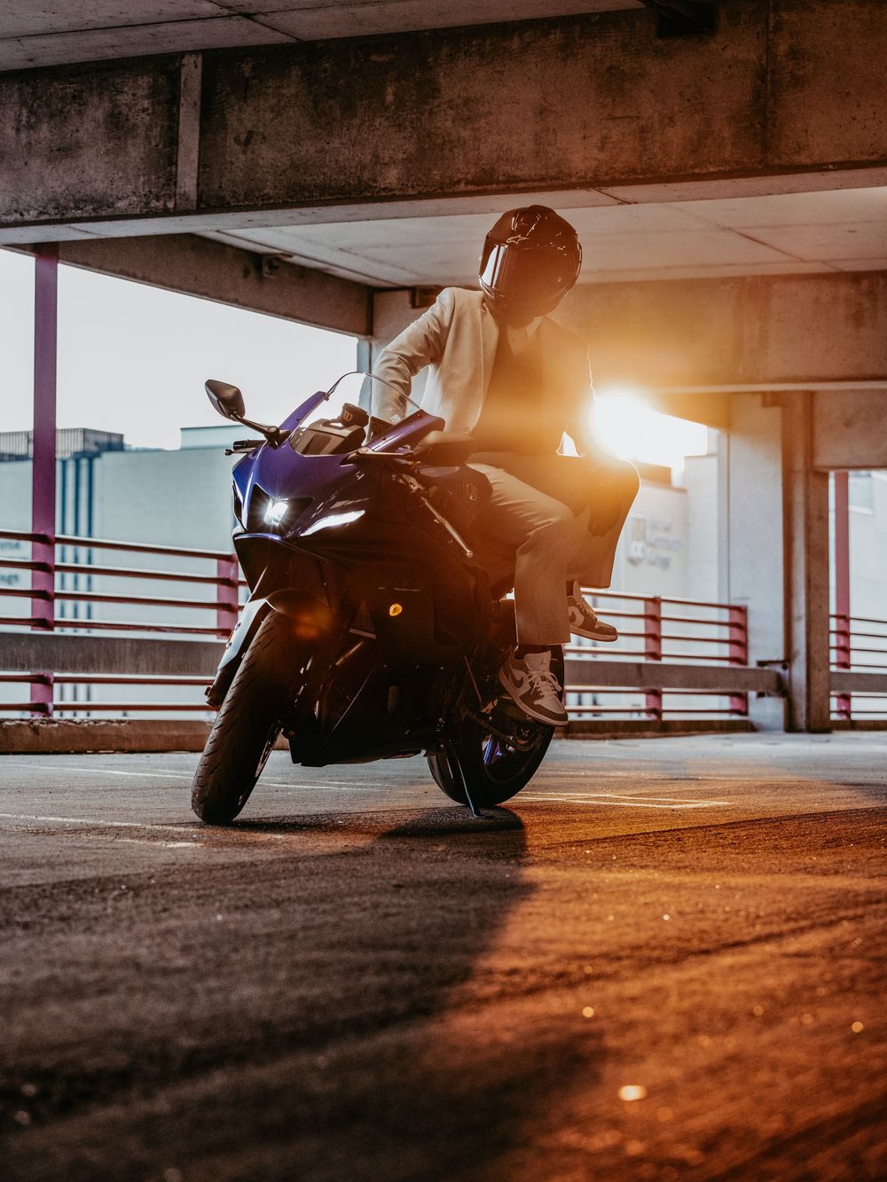 Motorcyclist in protective gear riding a sport bike in a parking garage at sunset with dramatic lighting.