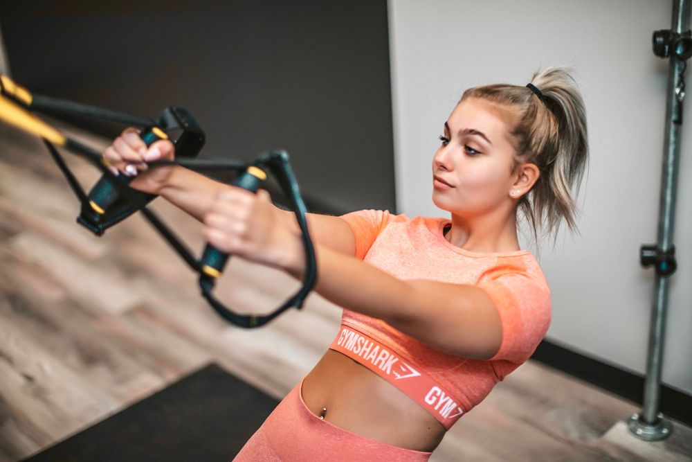 Person in coral workout top performing various TRX suspension training exercises in gym setting.
