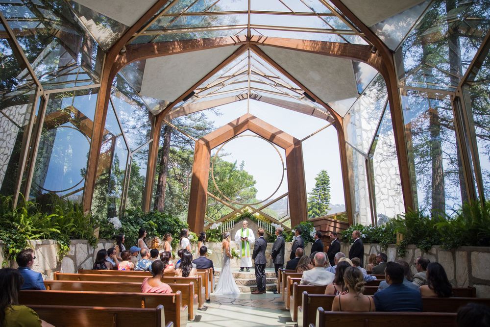 Wedding ceremony inside a stunning glass chapel with wooden pews and natural light streaming through.