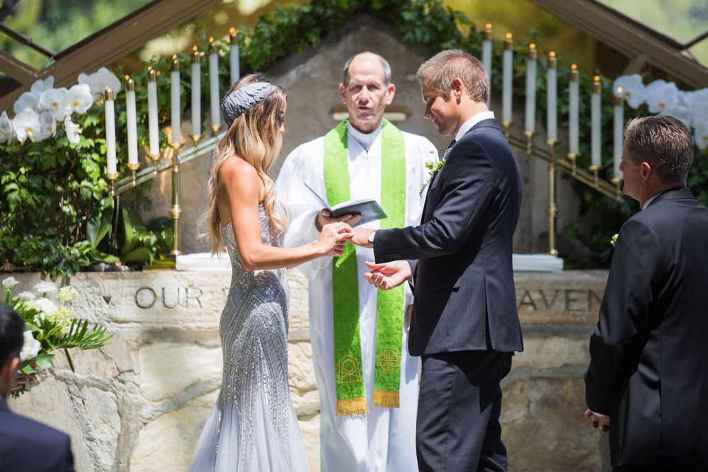 Bride and groom exchanging vows with officiant at an elegant outdoor altar adorned with white flowers.