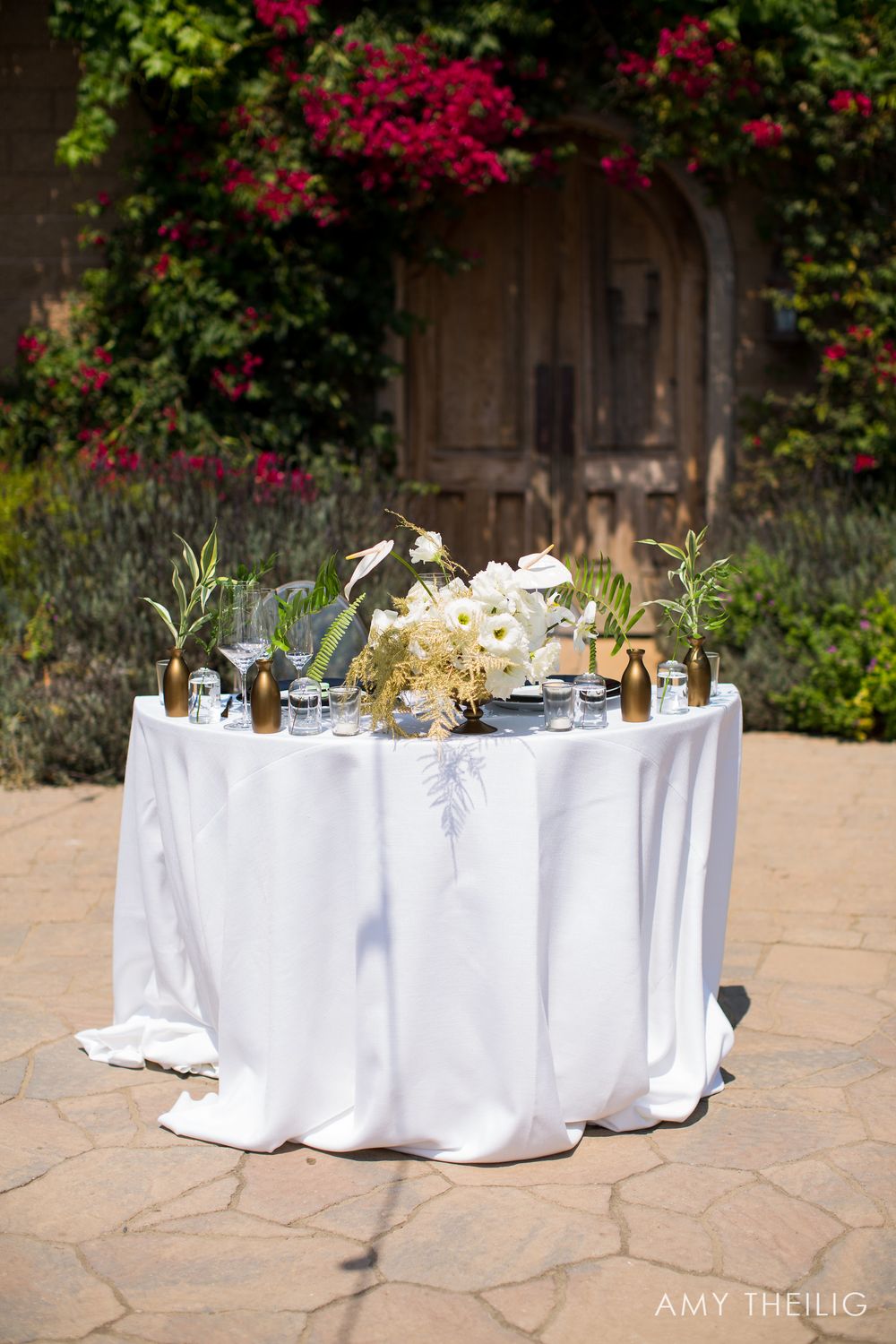 Elegant outdoor wedding sweetheart table with white linen, gold vases, and white floral centerpiece.
