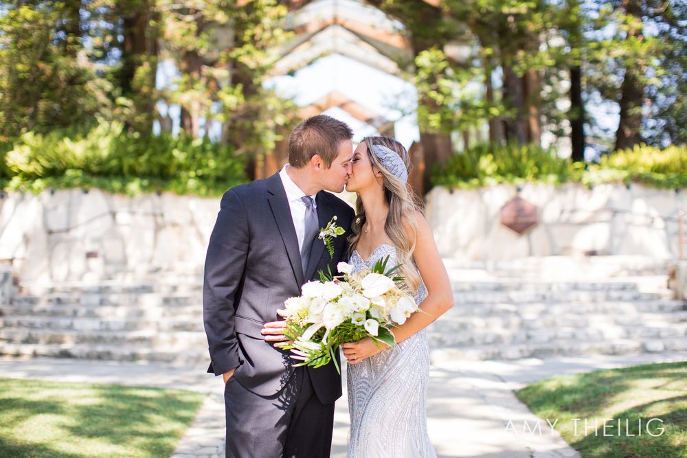 Bride and groom share a romantic kiss outside a stone wedding chapel.