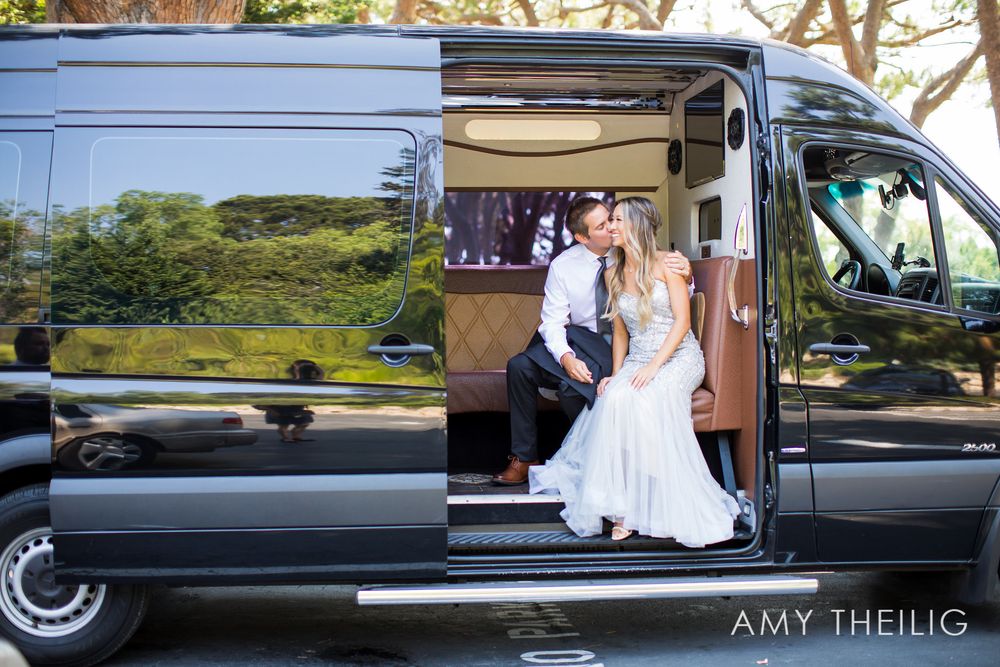 Newlyweds share a tender kiss seated in the open doors of a black luxury van.