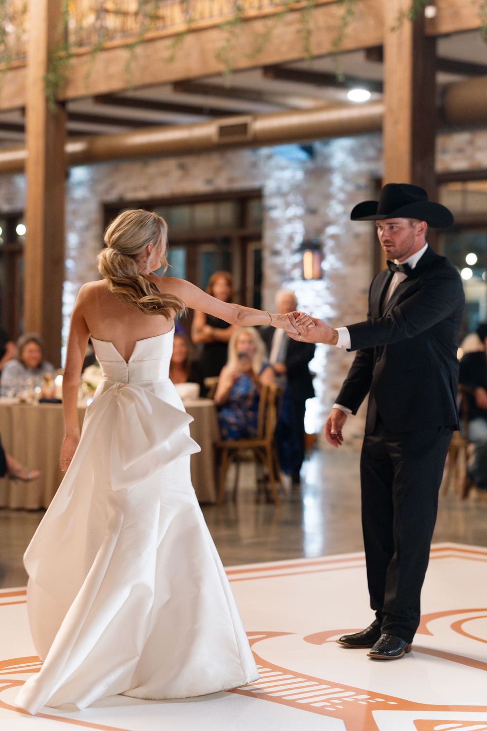 A couple shares their first dance at a wedding reception in a rustic venue with exposed brick walls and wooden beams.