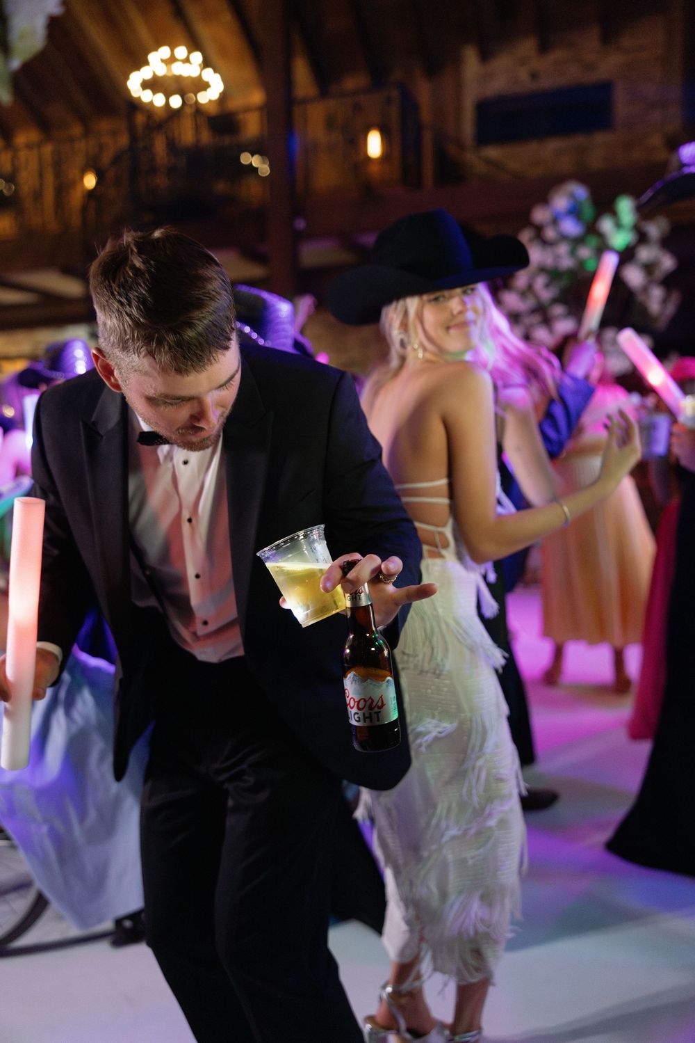 Wedding reception party on dance floor with colorful purple lighting and guests dancing and celebrating.
