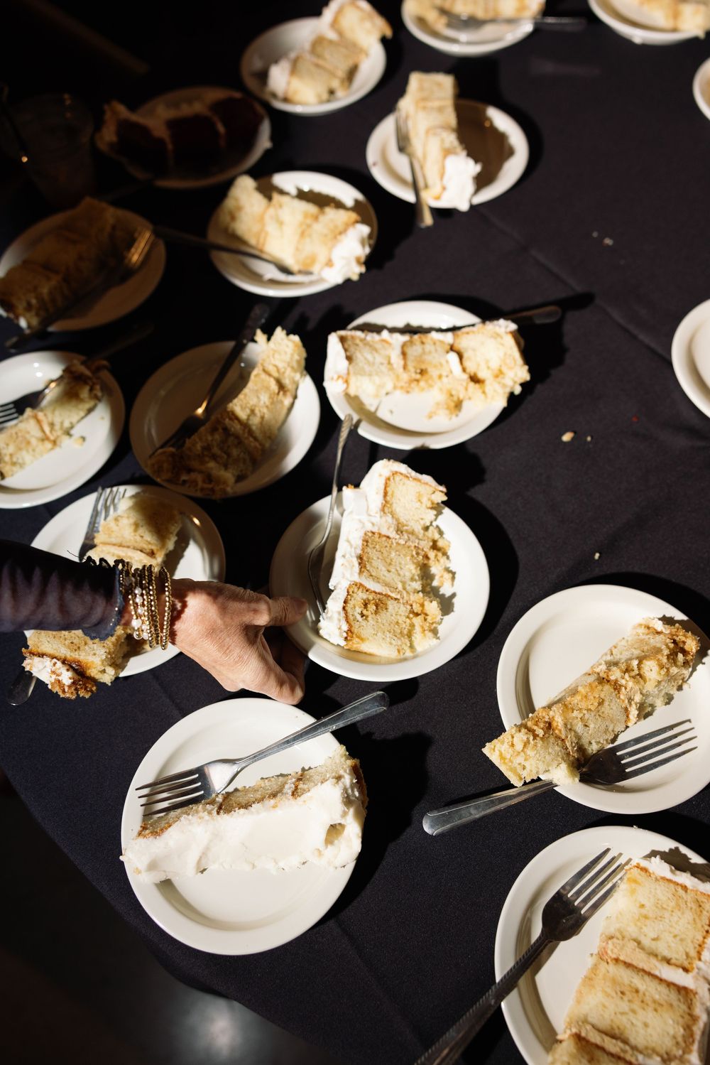 Slices of vanilla layer cake with white frosting served on small white plates with forks against a dark background.