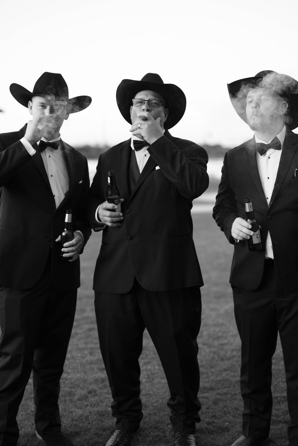 Three men in black suits and cowboy hats enjoying drinks together outdoors in a vintage black and white photo.