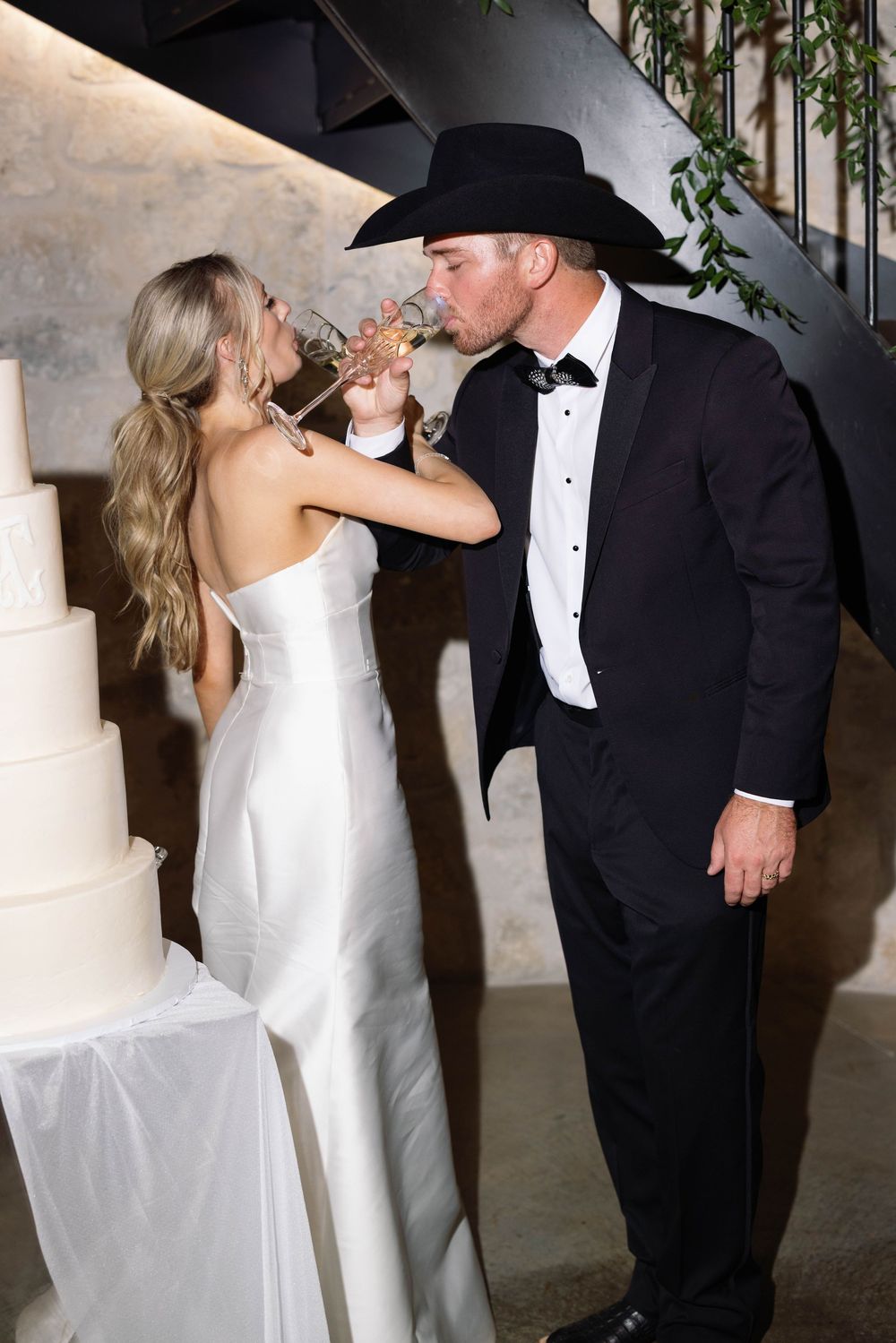 A bride and groom share a champagne toast at their wedding reception in formal attire.