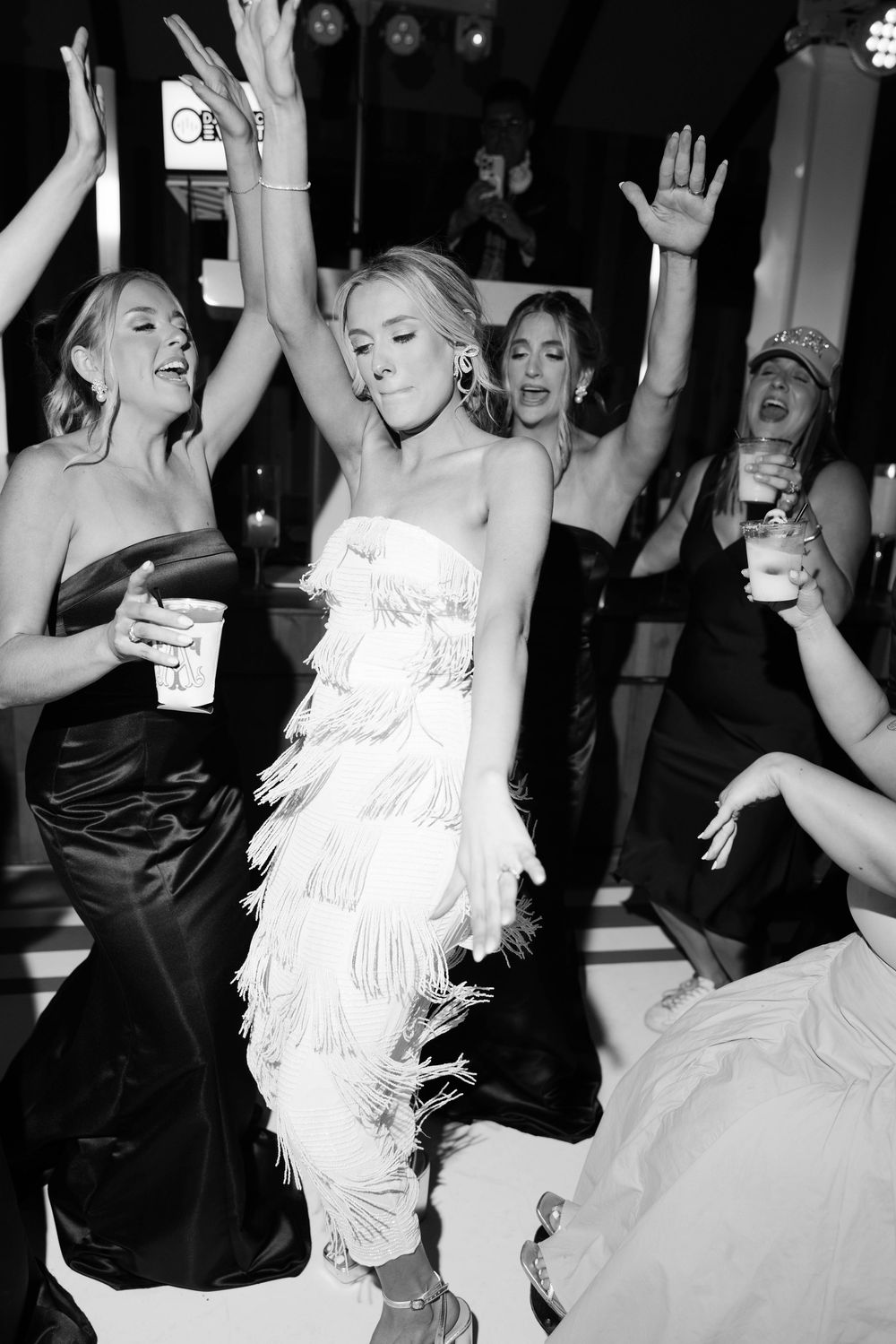 Black and white photo of people in formal attire dancing and celebrating at what appears to be a party or reception.