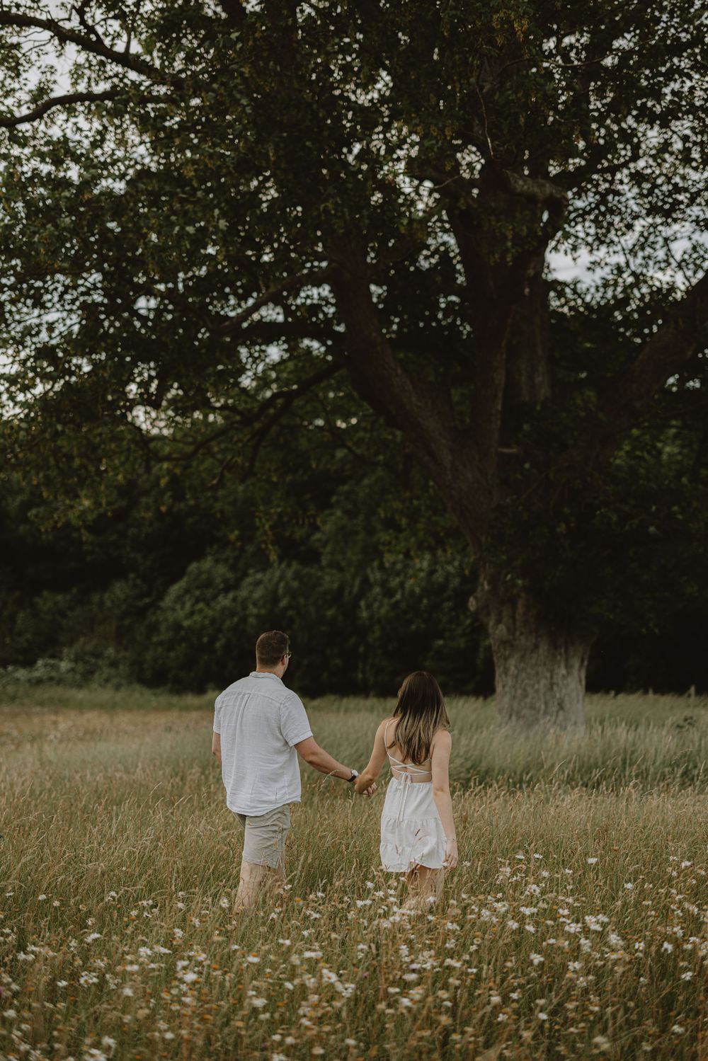 A romantic couple holding hands while walking through a wildflower meadow at sunset.