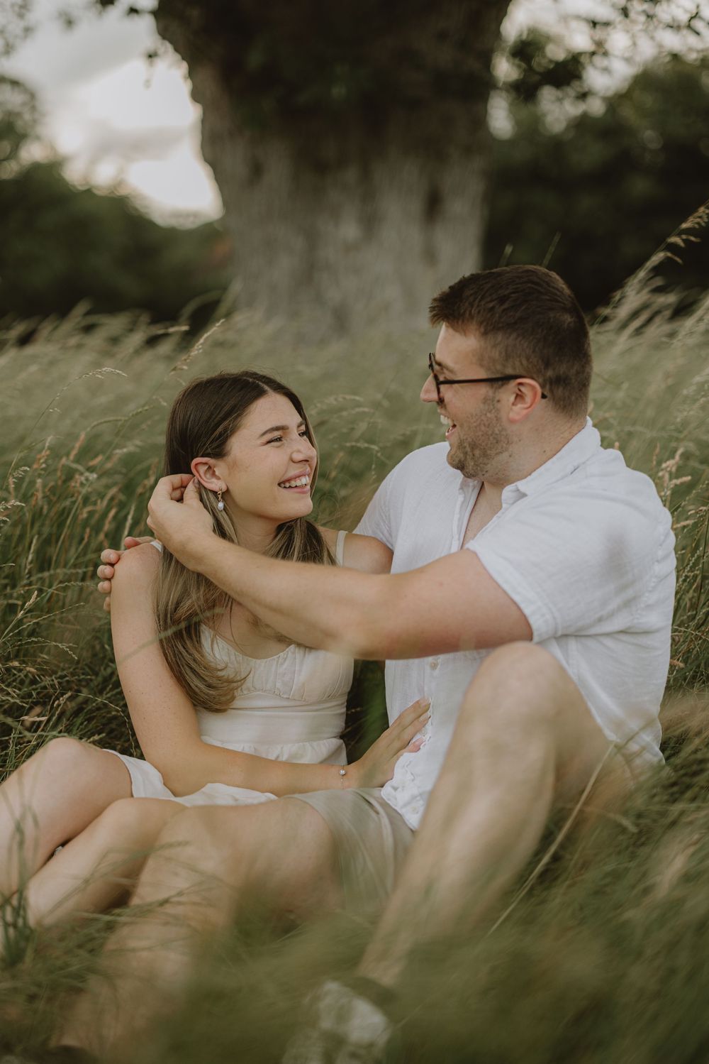 A couple shares a tender moment while sitting in tall grass during golden hour.