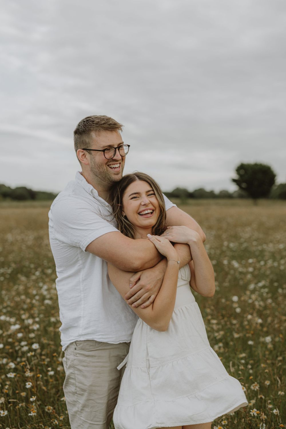 A joyful couple embraces while laughing together in a field of white wildflowers.