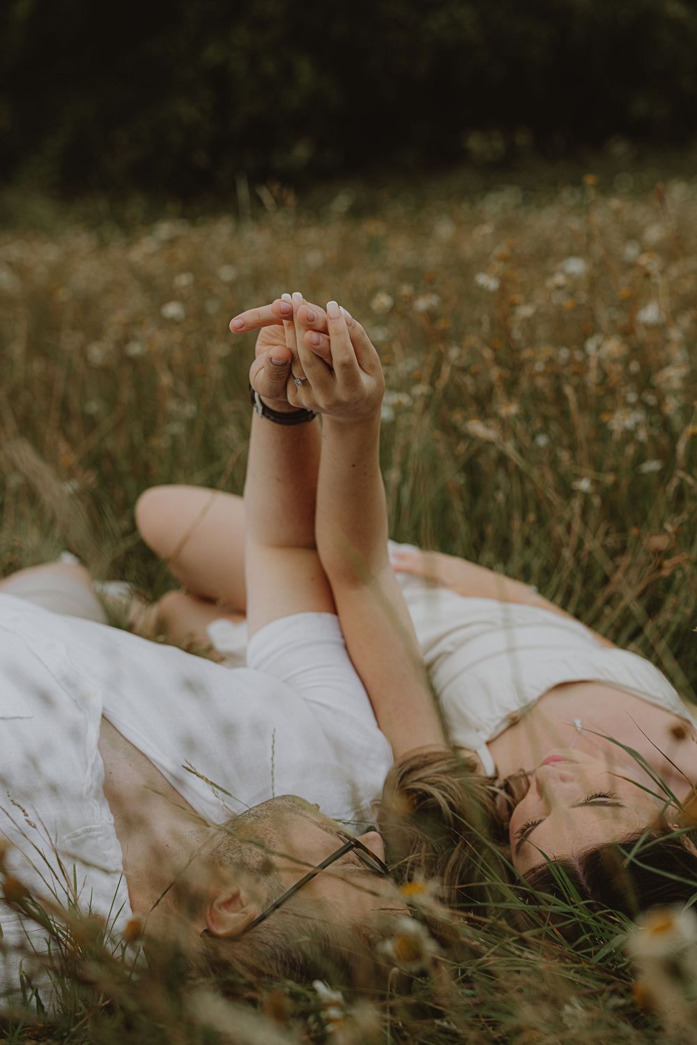 Two people lie peacefully in a wildflower meadow with their feet raised toward the sky.
