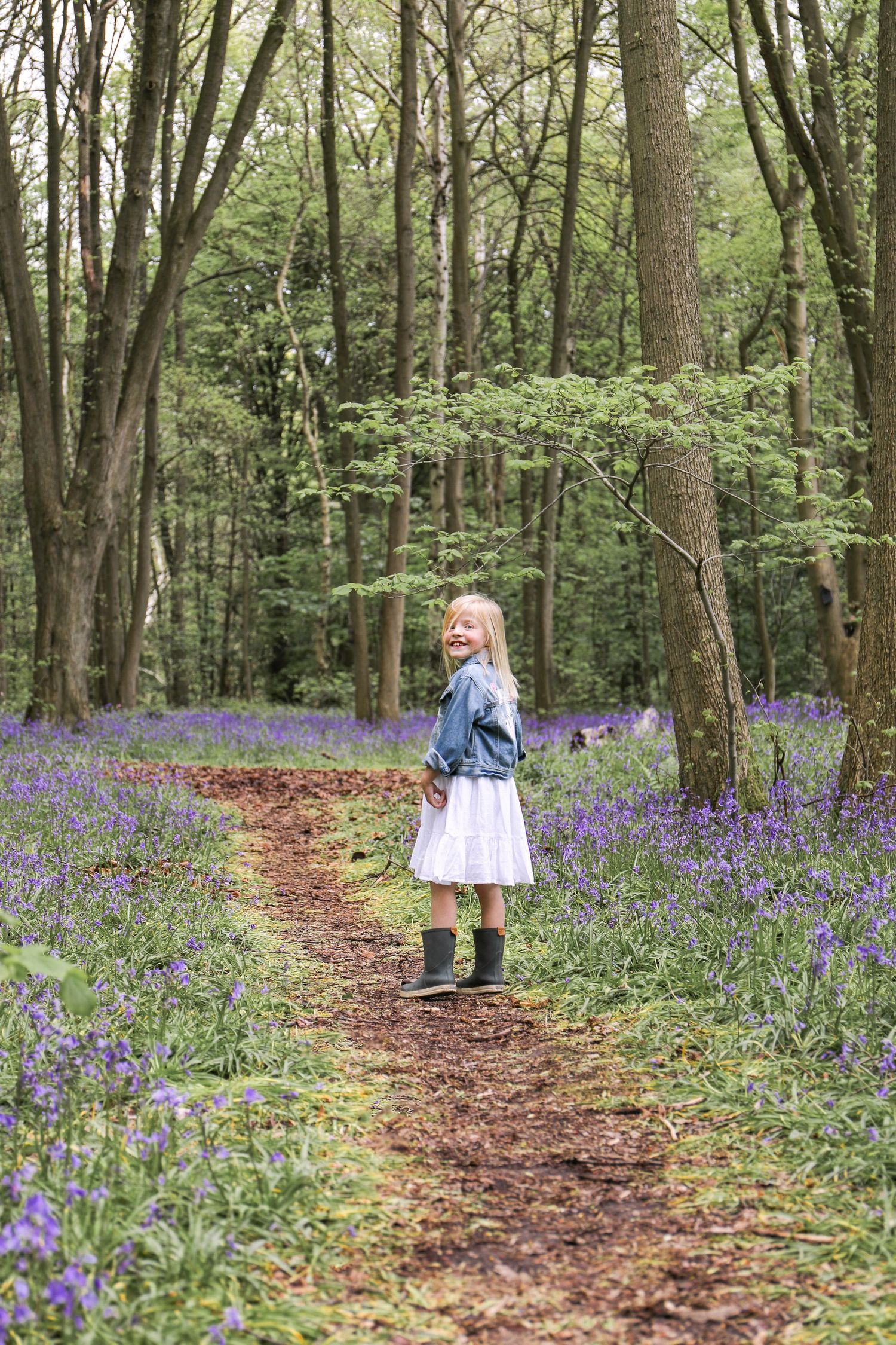 A girl stands amongst a scenic woodland path winds through a springtime forest filled with vibrant purple bluebells in bloom, Nottingham