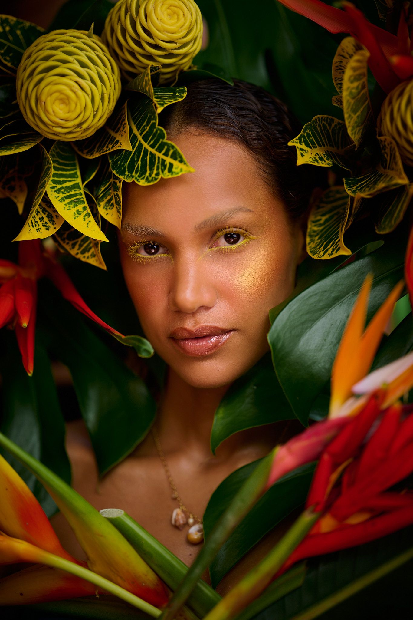 Close up portrait surrounded by vibrant yellow roses, tropical leaves, and red heliconia flowers in a garden setting.