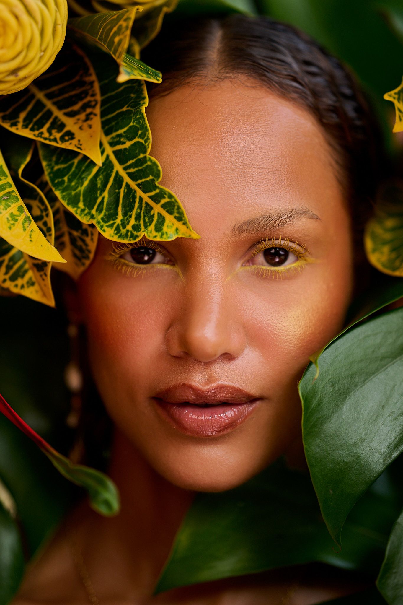 Artistic beauty portrait with yellow and green tropical foliage creating a natural frame against a dark background.