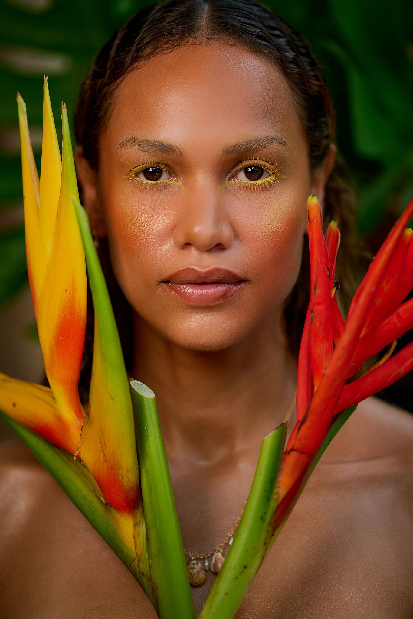 Vibrant heliconia flowers in red and yellow frame a sun-lit portrait against a lush green tropical background.
