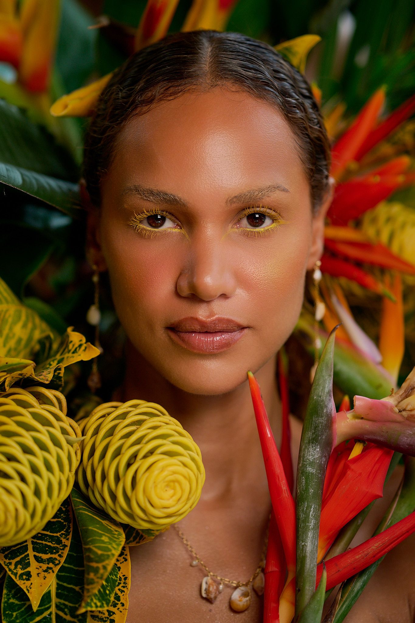 Fashion portrait with tropical flowers featuring heliconia and vibrant yellow fabric against a lush floral backdrop.
