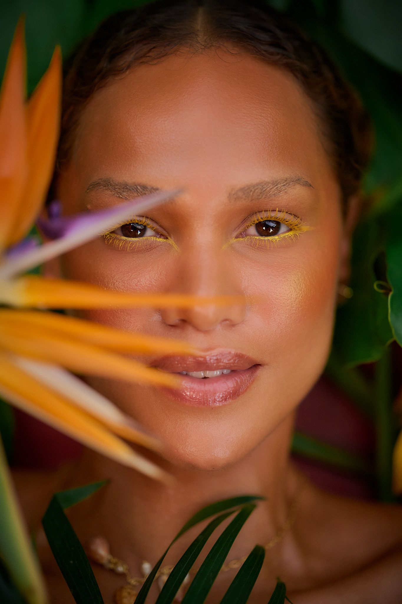 Close up portrait with bird of paradise flower petals and yellow eye makeup details in tropical setting.